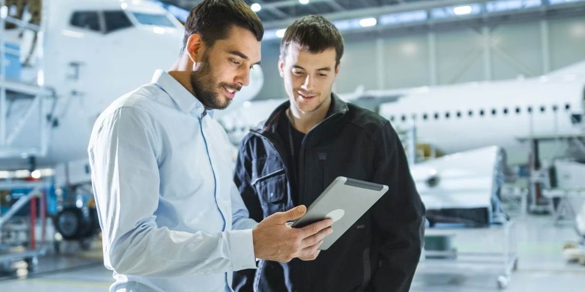 Two men looking at an ipad with an aeroplane behind them