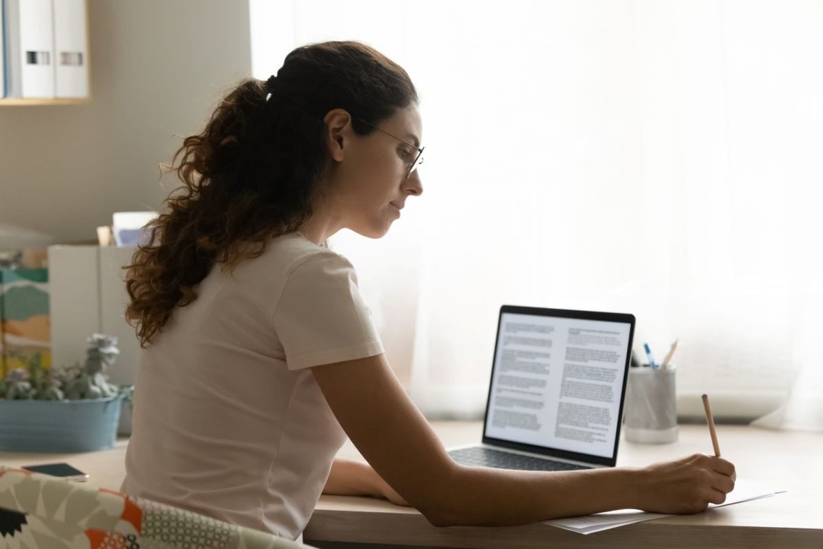 Woman taking notes at a desk with a laptop